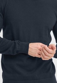 Marineblauwe trui gemaakt van zachte gebreide stof, met een ronde halslijn en geribbelde manchetten, waarbij handen de zoom aanpassen.