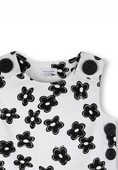 Robe blanche avec un motif floral noir, fabriquée en tissu lisse. Comprend de grands boutons noirs sur les épaules et une étiquette marquée.