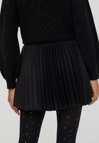 Gonna nera plissettata indossata con un maglione nero e collant neri, tutti decorati con piccoli punti argentati scintillanti.