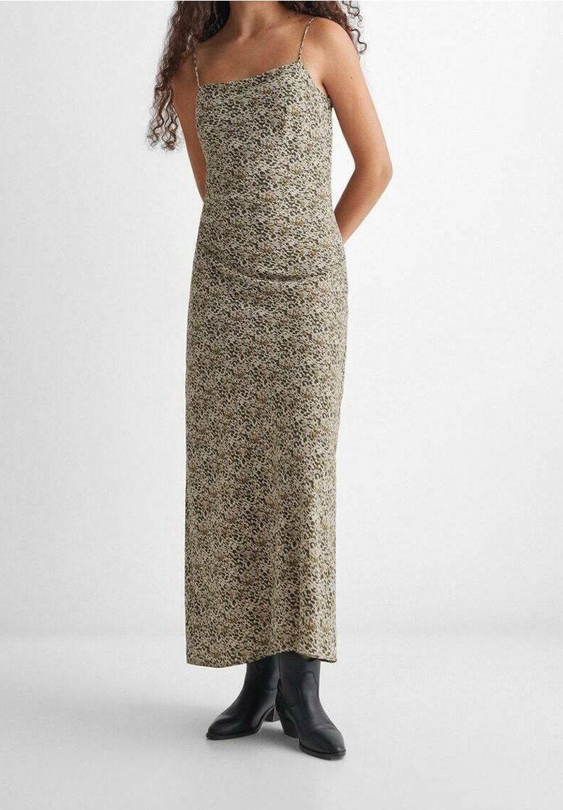 Femme portant une longue robe beige ajustée sans manches, avec un petit imprimé léopard noir et marron, associée à des bottines noires.