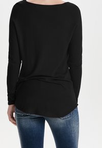 Maglietta nera a maniche lunghe con scollo ampio, vestibilità comoda e orlo arrotondato. Indossata sopra jeans in denim blu con un finish sbiadito.