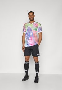 Multicolored athletic jersey with abstract patterns, short sleeves, and black shorts. Features Adidas branding and striped knee socks.