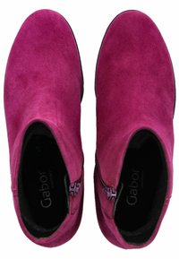 Botas de tobillo de ante fucsia con una textura suave, cierre de cremallera en el lateral y puntera redondeada. El interior presenta un detalle de marca.