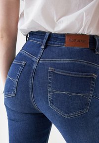 Tamno plave traperice s prilagođenim dizajnom, s dva stražnja džepa, kontrastnim šavovima i smešnim kožnim etiketom na kojoj piše "SALSA JEANS."