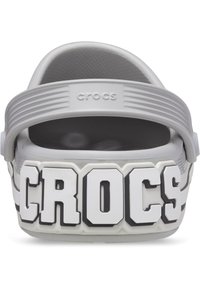 Zoccoli Crocs grigi con un grande logo bianco raffigurante "CROCS" sul davanti, interno texturizzato e strap posteriore regolabile per una migliore vestibilità.