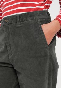Gray corduroy pants with a ribbed texture, featuring a side pocket and a button closure. Paired with a red and white striped long-sleeve shirt.