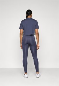 Jūras zila īsām piedurknēm saīsināta T-kreklu, saskaņota ar augsto jostasvietu jūras zila legingu un baltām kedām; gluda tekstūra, minimālisma dizains.