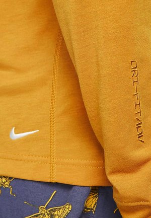 Tricou cu mânecă lungă Nike Dri-FIT de culoare muștar, cu un logo alb și detalii de text pe mânecă. Textură netedă și design ajustat.