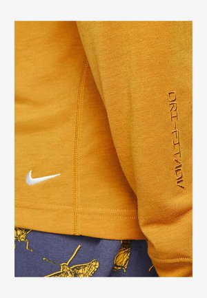 Nike Dri-FIT long-sleeve shirt in mustard yellow, featuring a white logo and text detail on the sleeve. Smooth texture and fitted design.