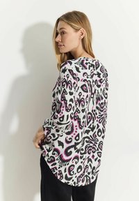 Långärmad blus i vitt med ett svart och rosa abstrakt mönster, med rundad nederkant och avslappnad passform, tillverkad av lättviktsmaterial.