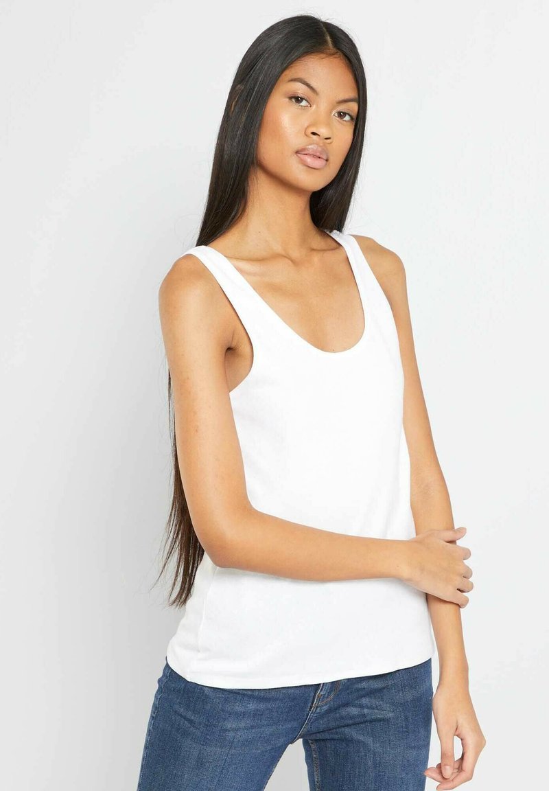 Biała bezrękawnikowa bluzka z okrągłym dekoltem, wykonana z lekkiego materiału. Zestawiona z niebieskimi dżinsami, które mają luźny krój.