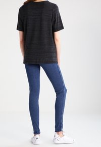 Black striped t-shirt with short sleeves paired with skinny blue jeans and white athletic shoes, viewed from the back.