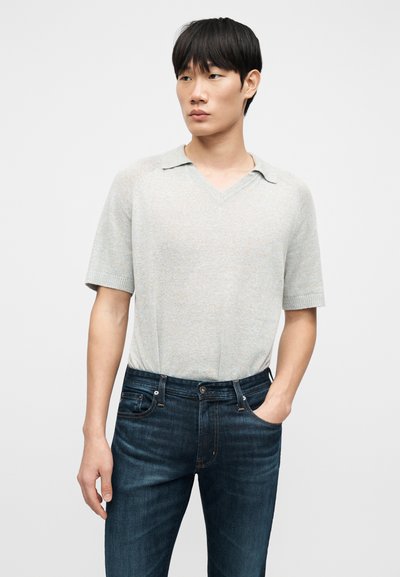 Ανοιχτό γκρι πουλόβερ με κοντά μανίκια και ντεκολτέ σε σχήμα V, με ριμπ γιακά, σε συνδυασμό με σκούρο μπλε τζιν. Το πουλόβερ έχει απαλή υφή και άνετη εφαρμογή.
