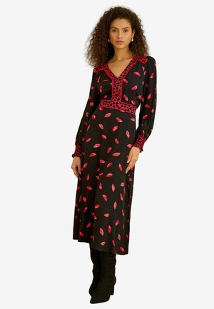 Sort langærmet kjole med røde bladmønstre og en kontrasterende, broderet halsudskæring. Stylet med høje sorte støvler.