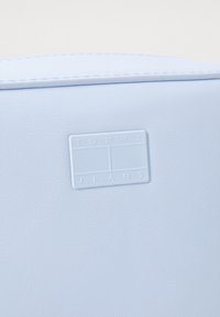Světle modrá taška z umělé kůže s texturovaným povrchem a obdélníkovou embosovanou visačkou s nápisem "TOMMY JEANS" v bílé barvě.