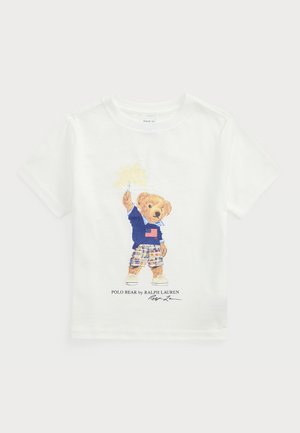 T-shirt de algodão branco com um urso de desenhos animados vestindo um suéter azul com a bandeira americana, calções xadrez e ténis, com o texto "POLO BEAR by RALPH LAUREN."