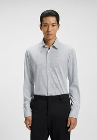 White long-sleeve shirt with a navy polka dot pattern, button-down collar, and smooth texture, paired with black textured pants.