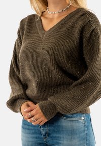 Maglione marrone a coste con scollo a V e maniche lunghe. Presenta pagliuzze dorate e una vestibilità comoda. Abbinato a jeans in denim blu chiaro.