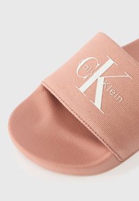 Ροζ σαγκάρι με υφή από μαλακό ύφασμα και λευκό λογότυπο. Η σόλα είναι από καλούπι καουτσούκ με ελαφριά γυαλάδα.