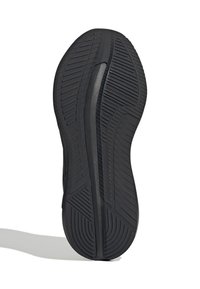 Semelle d'une chaussure de sport noire avec un motif de bande de roulement texturé et rainuré pour l'adhérence, vue de dessous sur fond blanc.