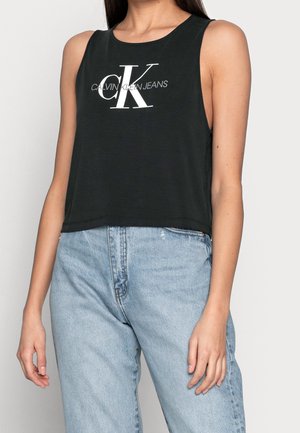 Czarny bezrękawnik typu crop top z okrągłym dekoltem, z białym logo "CK" na przodzie. Połączony z jasnoniebieskimi, wysokim stanem jeansami.