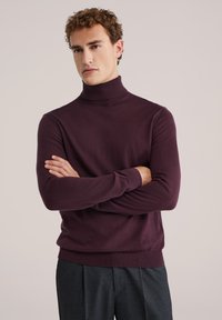 Temno vijolična turtleneck pulover z oprijetim krojem, rebrastim ovratnikom in manšetami, nosi s temnimi strukturiranimi hlačami.