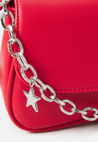 Rode leren handtas met een zilveren kettingband met ovale schakels en een stervormige hanger. Gladde textuur en gestroomlijnd ontwerp.