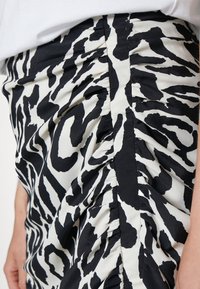 Jupe à motif zèbre noir et blanc en tissu lisse, avec des détails froncés sur le côté et une coupe ajustée.