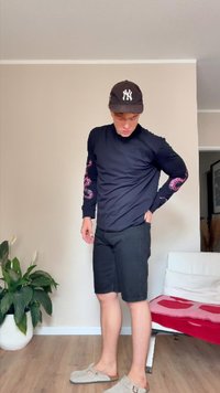T-shirt noir à manches longues avec graphique de dragon rose sur les manches, associé à un short noir et des chaussures à enfiler gris clair. Environnement intérieur.