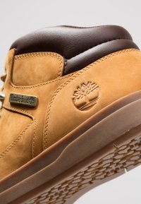 Hellbraune Leder-Sneaker mit einem gepolsterten Kragen in Braun, ausgestattet mit einem geprägten Logo, einem goldfarbenen Markenschild und einer strukturierten Gummisohle mit einem Wabenmuster.