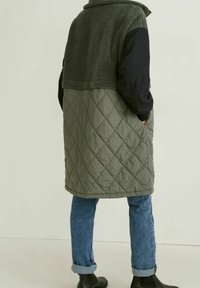 Chaleco acolchado verde oliva con parte superior de felpa verde oscuro y mangas negras, con bolsillos laterales y dobladillo curvo.