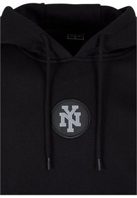 Zwarte hoodie met een ronde zwarte patch met een grijze 'NY'-logo. Gemaakt van zacht materiaal met trekkoorden aan de capuchon.
