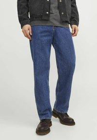 Jeans de mezclilla azul con corte relajado, que presentan un diseño de pierna recta y costuras clásicas. Combinados con botas de color marrón oscuro.