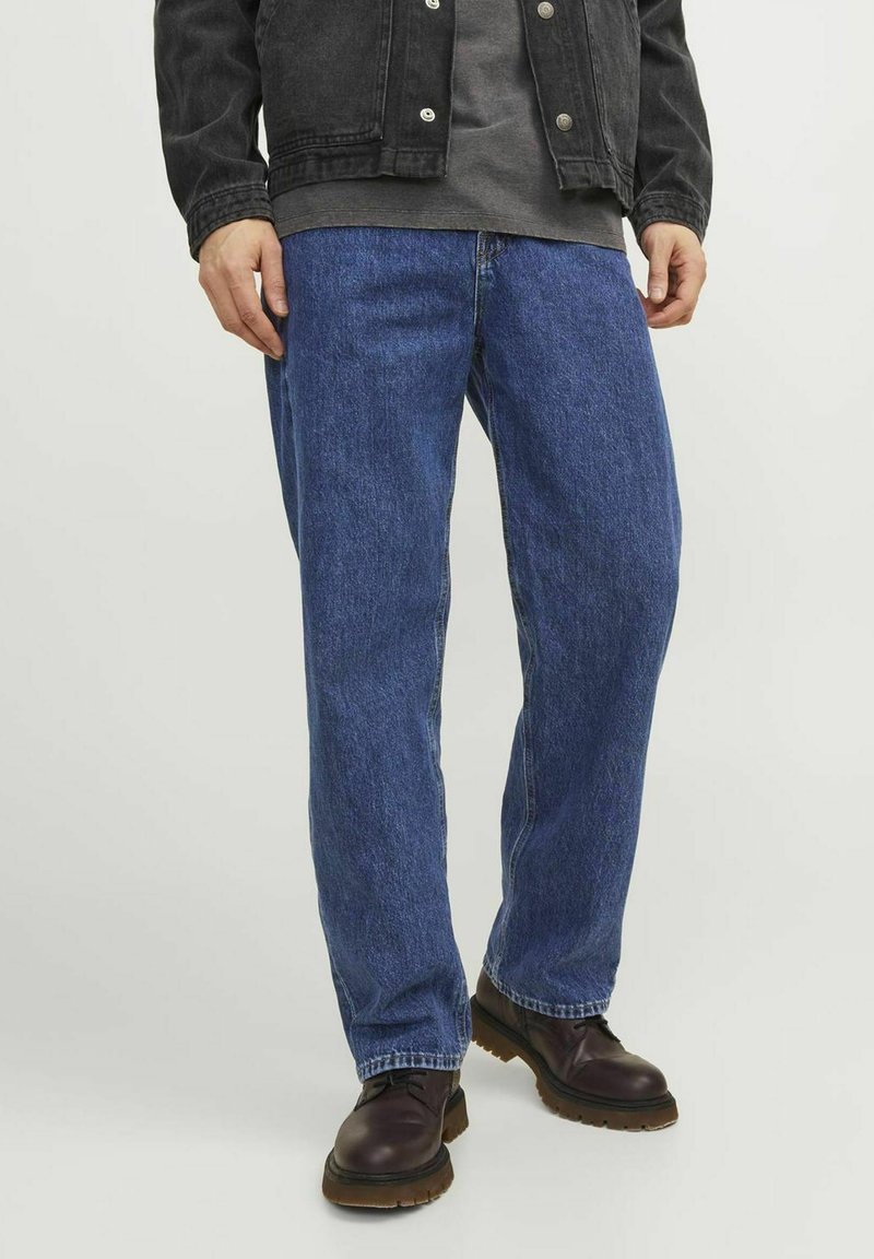 Jeans de mezclilla azul con corte relajado, que presentan un diseño de pierna recta y costuras clásicas. Combinados con botas de color marrón oscuro.