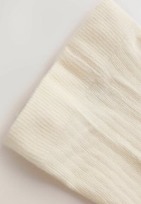 Primer plano de tela de punto acanalado color crema que muestra puntadas texturizadas y material suave.