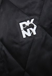 Logo abstrait blanc avec des lettres superposées P, K, N, Y et une forme de cœur sur un fond en tissu matelassé noir.