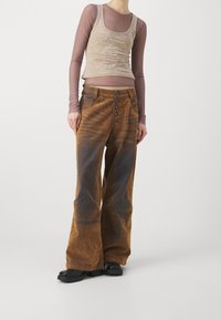 Bruna vida-byxor i kordflossa med femknapprad, som har subtila ränder och kontrasterande textur. Åtföljd av en beige figurnära linne.