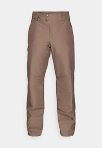 Hnedé vonkajšie nohavice s hladkým povrchom, dvoma zapínaniami na gombíky a bočnými zipsami pre vrecká. Obsahujú zosilnené kolená pre väčšiu odolnosť.