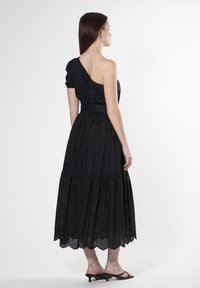 Vestido negro de un solo hombro, con manga corta abullonada, diseño en capas, detalles bordados y dobladillo con forma de ondas, combinado con sandalias negras de tacón.