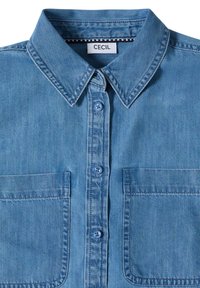 Chemise en denim bleu clair à boutons, col pointu, deux poches poitrine, et étiquette de marque "Cecil" à l'intérieur du col.