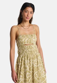 Φόρεμα ανοιχτού πράσινου με λουλουδάτο σχέδιο, ελαστική κορυφή με πιέτες και λεπτές τιράντες. Διαθέτει άνοιγμα κάτω από το στήθος και απαλότητα υφής.