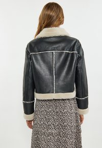 Zwarte leren jas met witte schapenvachtkraag en -afwerking, cropped ontwerp, horizontale stiknaden en een gladde textuur.