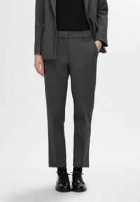Pantalon gris ajusté en tissu texturé, coupe slim, poches avant inclinées et ourlet propre, associé à des chaussures noires à lacets.