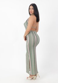 Pasiasty kombinezon w kolorach zielonym, różowym i białym; z dekoltem na szyi; z odkrytymi plecami; z rozcięciami po bokach; w połączeniu z białymi szpilkami.