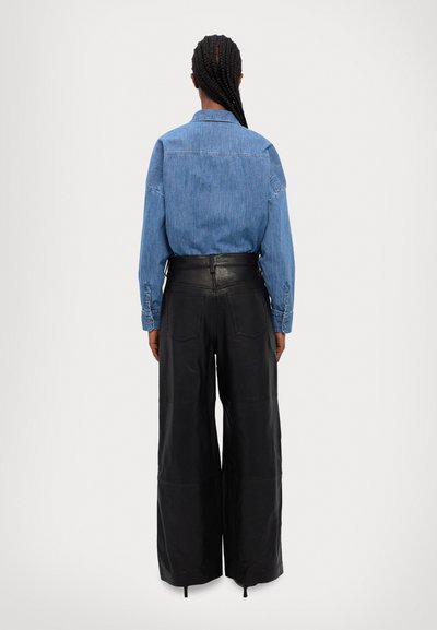 Denim-paita, jossa on vaaleansininen pinta, napitettu hiha, yhdistetty laajoihin mustiin nahkahousuihin, joissa on korkea vyötärö ja takataskut.