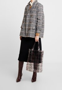 Dvojřadý kostičkovaný kabát v černé, bílé a broskvové barvě, kombinovaný s černou sukní a průhlednou taškou s kostičkovaným vzorem.