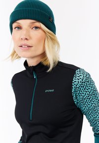 Zwarte rits-top met teal accenten en gebloemde mouwen. Het materiaal lijkt rekbaar, wat zorgt voor een nauwsluitende pasvorm. Inclusief logo op de borst.