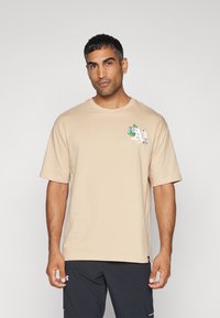 Camiseta de algodón beige de manga corta, con cuello redondo y un gráfico de flores colorido en el pecho. Textura suave, corte relajado.