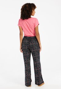 Roze top met korte mouwen gecombineerd met kleurrijke, flared broeken met een bloemenpatroon op een donkere achtergrond.