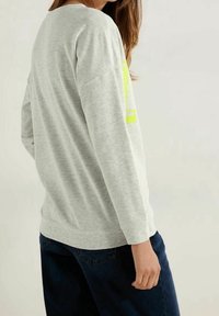 Camisa de manga larga en gris claro, hecha de un material suave, con un diseño gráfico en neón amarillo intenso en la parte frontal y un corte relajado.
